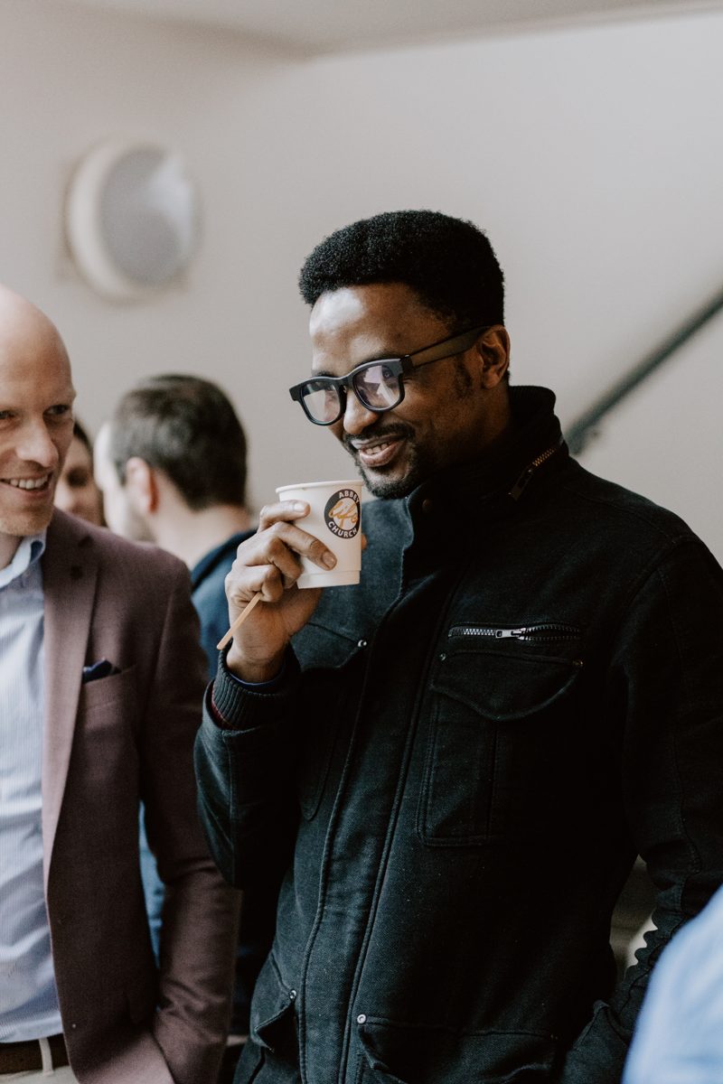 Marcus Oyelaran smiling with a coffee among friends
